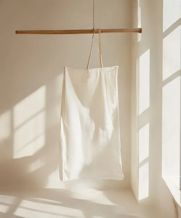 Hellweißer Kleidersack hängt an einer Holzstange im Tageslicht eines Studios