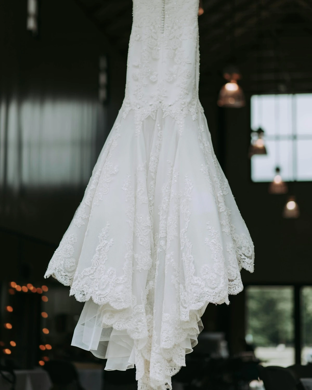 Ein Brautkleid hängt in einem warmen Licht — fließender Mermaid-Schnitt, dreidimensionale Blütenstickerei, scalloped Spitzensaum